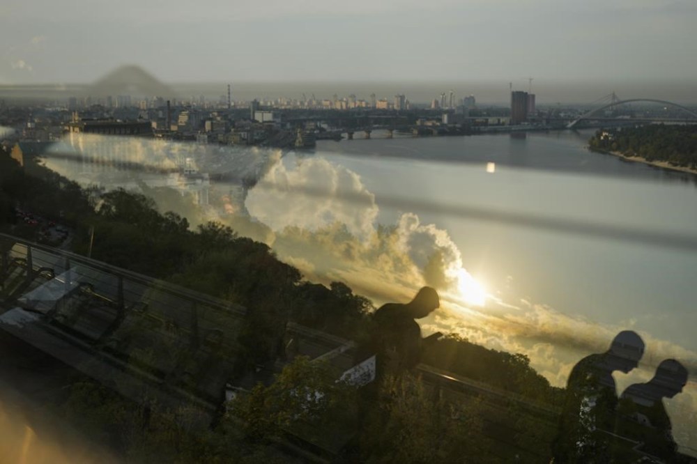 Pedestrians are reflected in a security glass as they walk along the Glass Bridge over the Dnipro river in Kyiv, Ukraine, Friday, Sept. 30, 2022. (AP Photo/Francisco Seco)