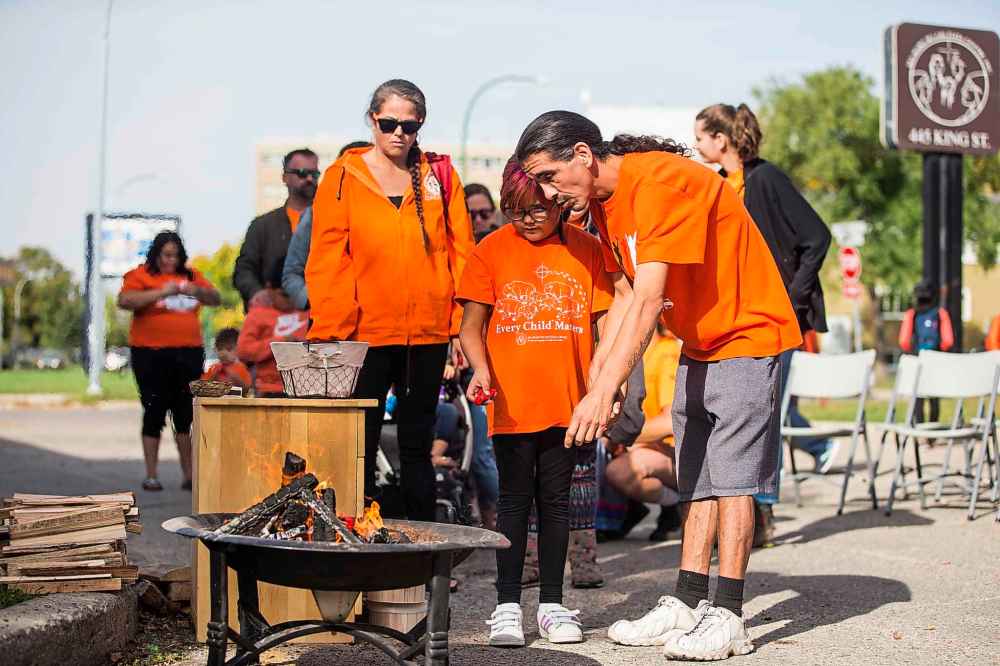 Maurice Fontaine and his daughter, seven-year-old Rylynn Lefort, throw tobacco ties into the sacred fire at Ma Mawi Wi Chi Itata Centre on Friday. (Mikaela MacKenzie / Winnipeg Free Press)