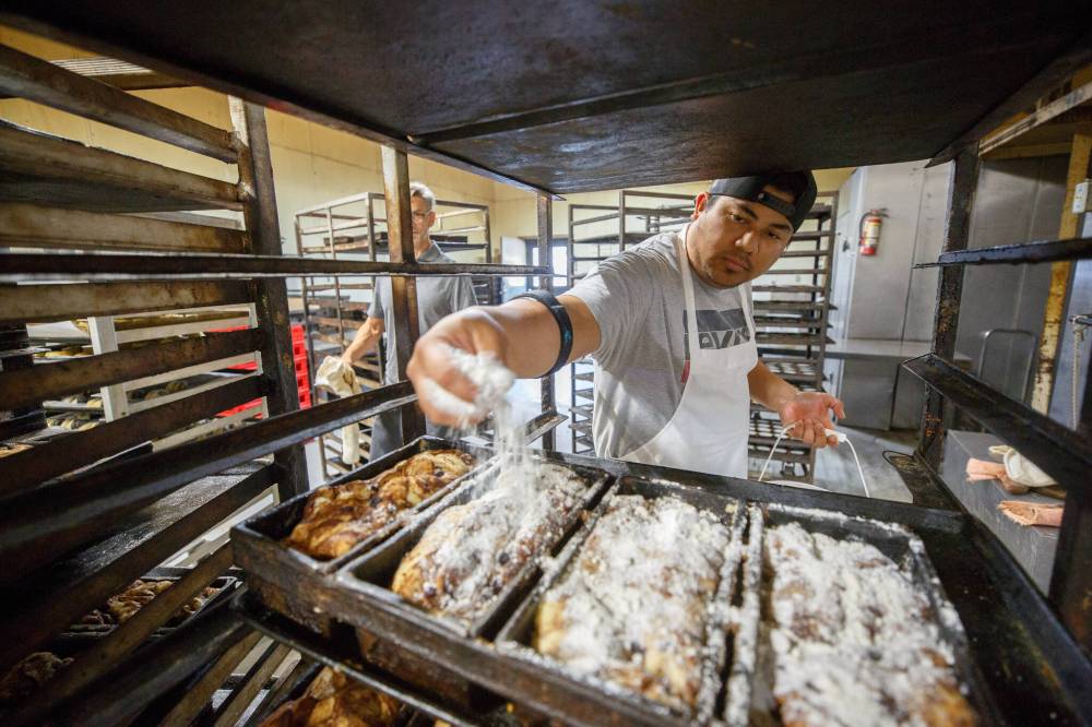 Baker Lester Villa sprinkles a mixture that includes margarine, pastry flour and fine sugar, onto loaves of apple cinnamon bread that have come out of the proofing oven, before being put into the huge oven to bake.
