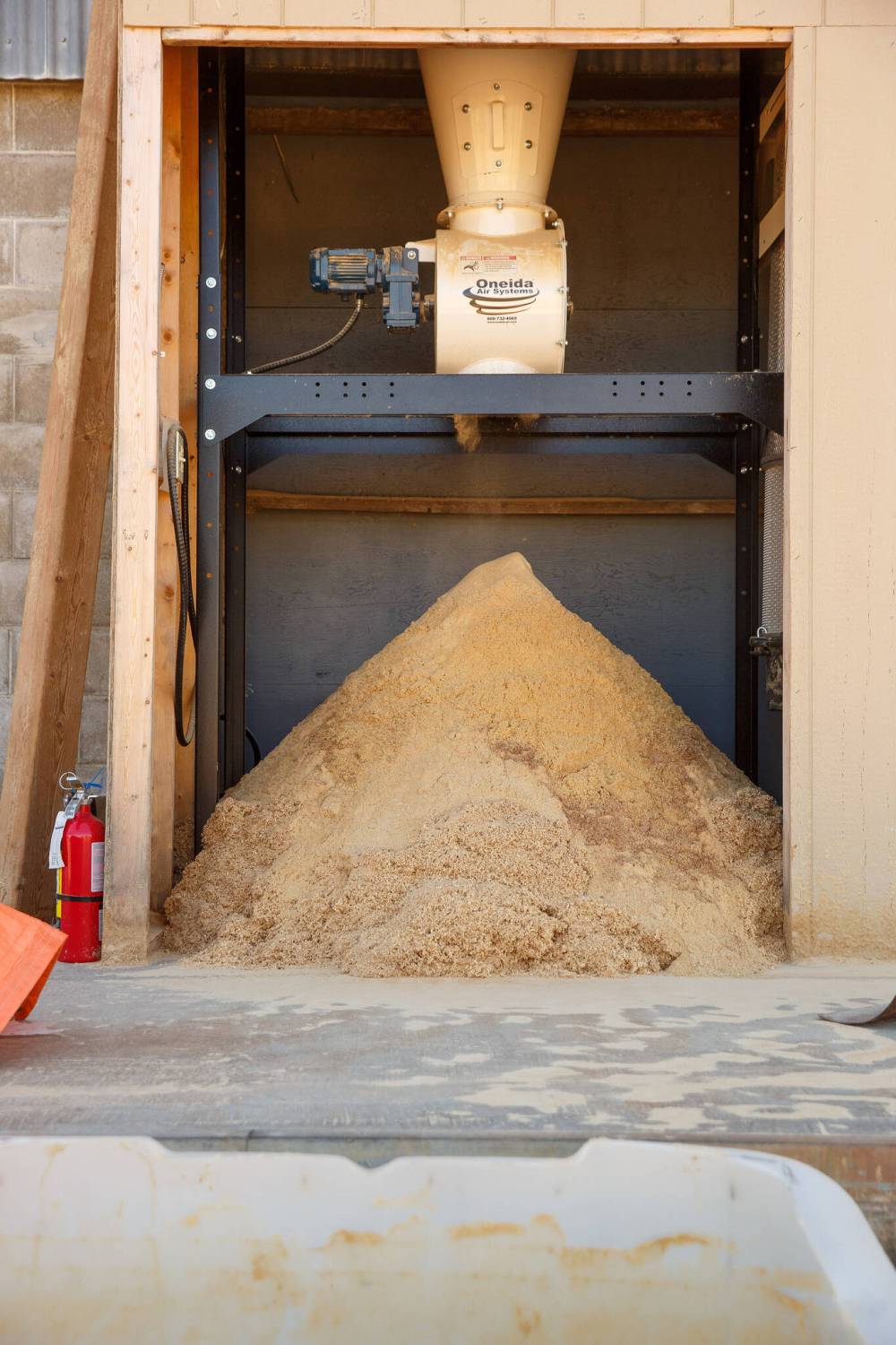 A pile of sawdust sits under a vent from the milling machines inside.