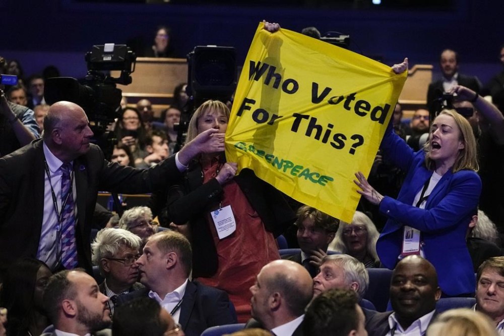 FILE - A man pulls down a banner held by two protesters as Britain's Prime Minister Liz Truss makes a speech at the Conservative Party conference at the ICC in Birmingham, England, Wednesday, Oct. 5, 2022. Truss has only been in office for six weeks. But already her libertarian economic policies have triggered a financial crisis, emergency central bank intervention, multiple U-turns and the firing of her Treasury chief. (AP Photo/Kirsty Wigglesworth, File)