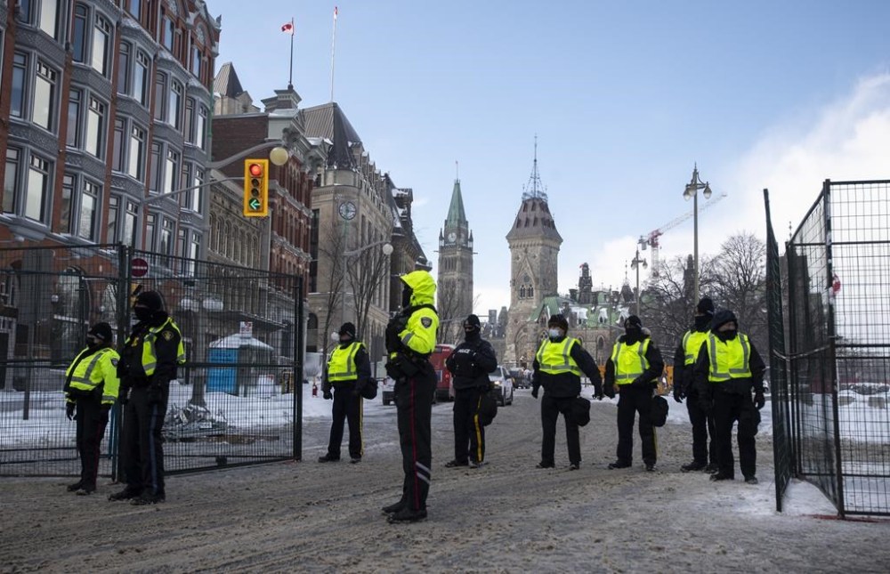 The Peace Tower is seen behind police at a gate along Queen Street as they restrict access to the streets around Parliament Hill in Ottawa, Saturday, Feb. 19, 2022. The inquiry into the federal government's use of the Emergencies Act during February's