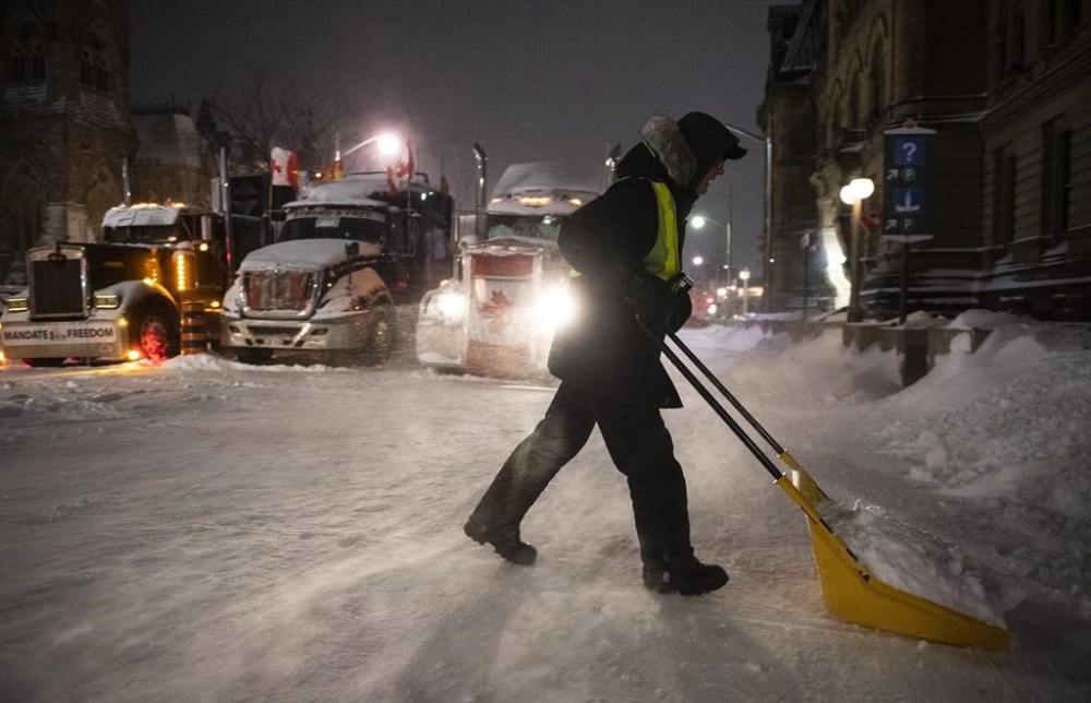 A protester shovels snow from Wellington Street in front of a blockade of trucks as a winter storm warning is in effect, on the 22nd day of a protest against COVID-19 measures that has grown into a broader anti-government protest, in Ottawa, on Friday, Feb. 18, 2022. The commission investigating the federal government's invocation of the Emergencies Act says most of the millions of dollars raised by the
