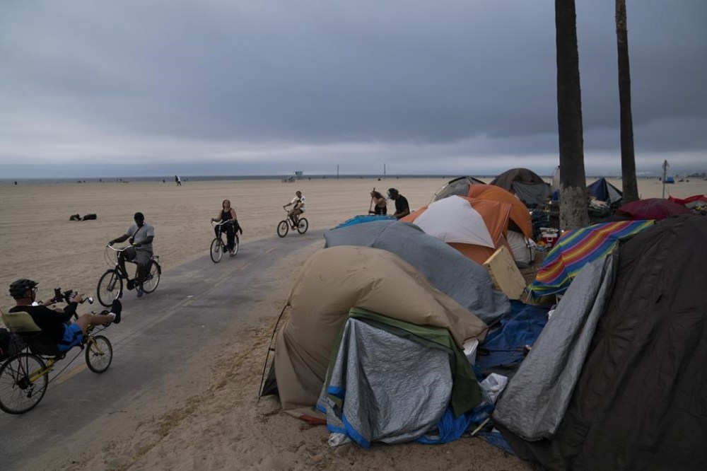 FILE - People ride their bikes past a homeless encampment set up along the boardwalk in the Venice neighborhood of Los Angeles on June 29, 2021. California Gov. Gavin Newsom said Thursday, Nov. 3, 2022, he will delay $1 billion of spending to local governments because he says they are not being aggressive enough to curb homelessness in their communities. (AP Photo/Jae C. Hong, File)