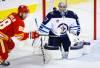 Winnipeg Jets goalie Connor Hellebuyck, right, follows the puck as Calgary Flames forward Elias Lindholm tries to get his stick on it during third period NHL pre-season hockey action in Calgary, Friday, Oct. 7, 2022.THE CANADIAN PRESS/Jeff McIntosh