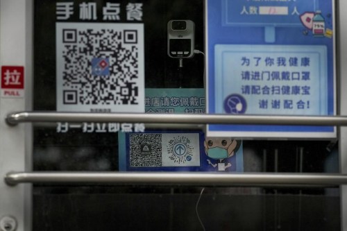 A temperature scanner stands near a display note showing a health check and travel QR codes at a closed fast-food restaurant in Beijing, Monday, Dec. 12, 2022. China will drop a travel tracing requirement as part of an uncertain exit from its strict 
