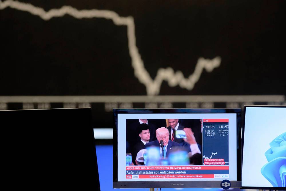 Michael Probst / The Associated Press files
The curve of the German stock index DAX is seen in the background as U.S. President Donald Trump is shown on a TV screen at the stock market in Frankfurt, Germany.