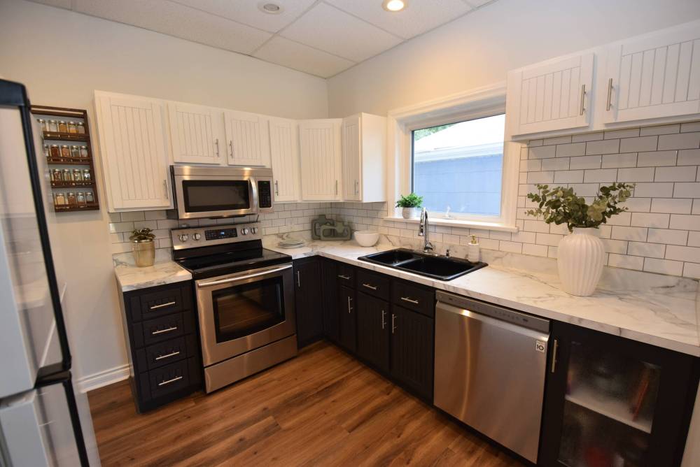 The roomy, updated kitchen has two-tone cabinets, a tile backsplash, stainless range and dishwasher and a double sink with mod faucet.