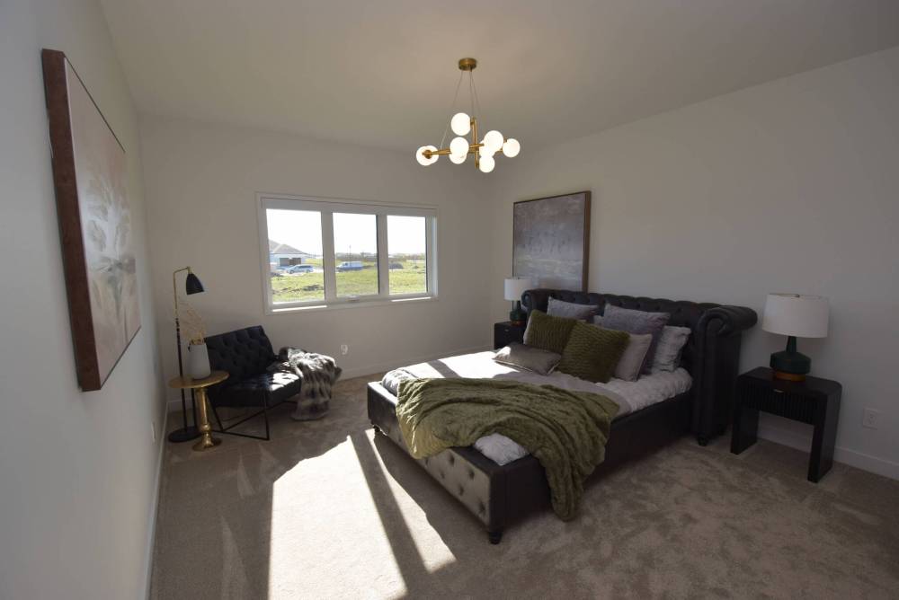 An air of calm pervades the privately positioned primary bedroom.
Todd Lewys / Free Press
A nine-foot island with matte-black porcelain countertop, waterfall sides and warm woodgrain-style cabinetry serves as the anchor point of the elegantly understated kitchen in Artista Homes’ spacious bungalow in Forest Grove Estates.