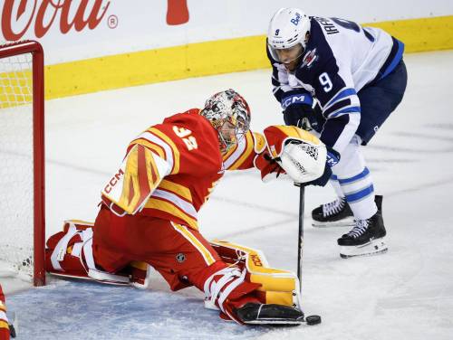Jeff McIntosh / THE CANADIAN PRESS
                                Jets forward Alex Iafallo (right) tries to poke the puck past Flames goalie Dustin Wolf on Monday night in Calgary.