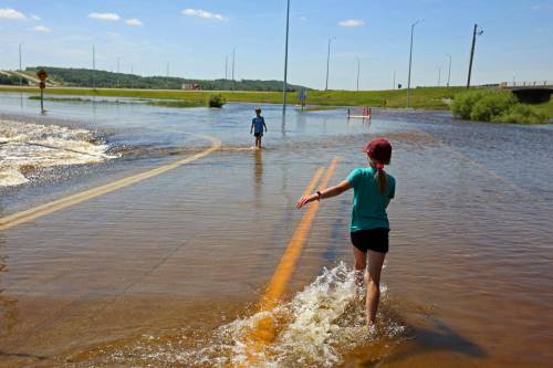 Tim Smith/The Brandon Sun
                                Brooks and Emily Zamrykut wade in the flood waters of the Assiniboine River pouring over Grand Valley Road near the Trans Canada Highway in Brandon on a scorching hot Monday afternoon.